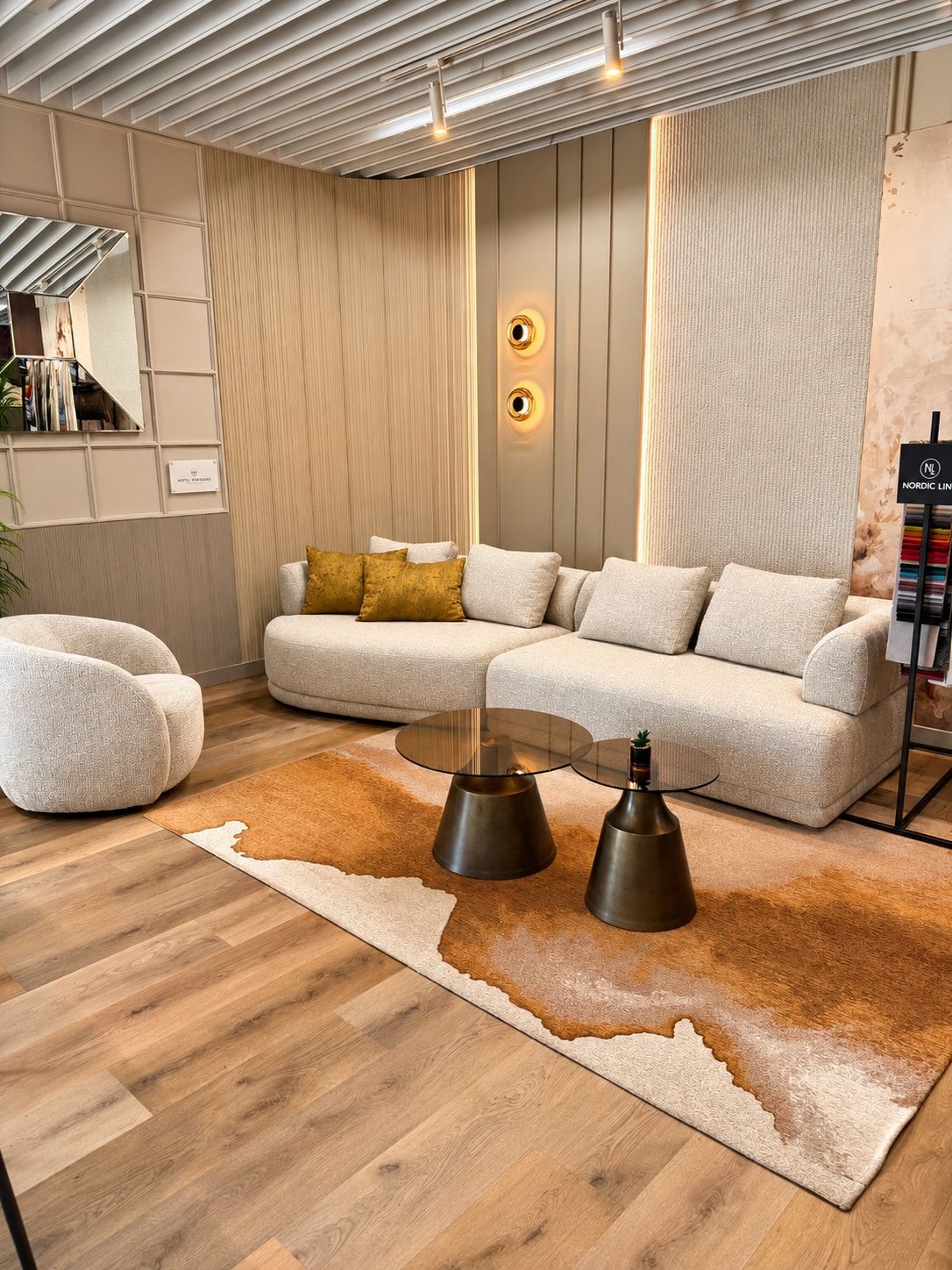 Jasna sofa o zaokrąglonej formie, okrągły fotel i dwa metalowe stoliki na dywanie w bieli i rudym