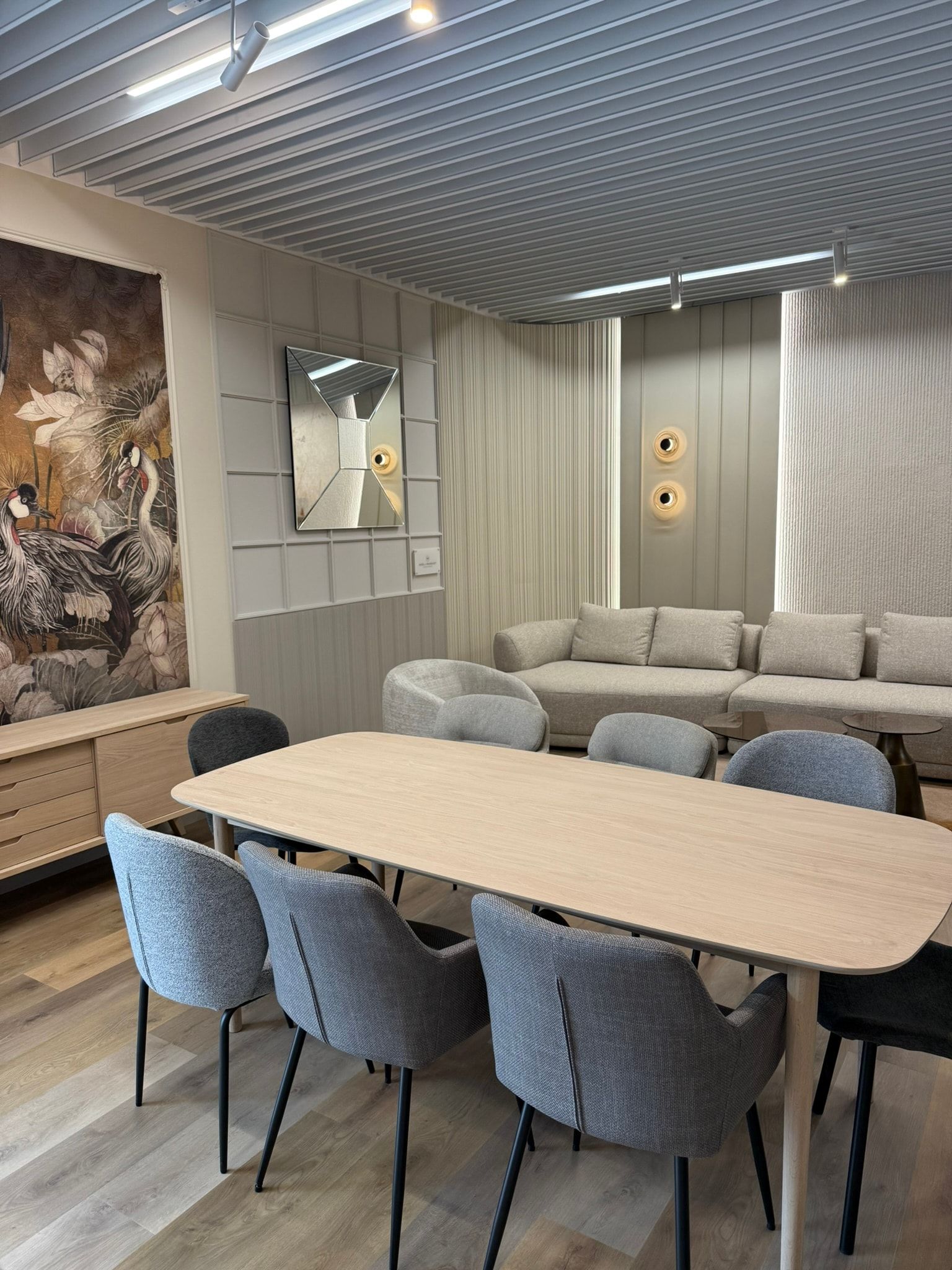 Jasny drewniany stół z szarymi tapicerowanymi krzesłami, w tle jasna sofa i fotel